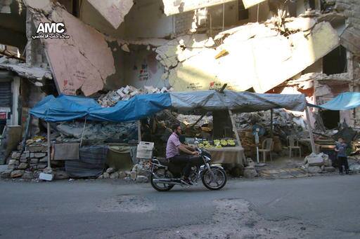 In this Friday, July. 29, 2016 photo, provided by the Syrian anti-government activist group Aleppo Media Center (AMC), shows a Syrian man rides a motorcycle passes by a damaged building that was destroyed by airstrikes in Aleppo, Syria. Residents trapped in rebel-controlled Aleppo are struggling to survive the crippling encirclement of their once thriving city. Bread, medication and fuel are running short. For the tens of thousands who chose to remain, the battle for Aleppo is a pivot point in the Syrian war. (Aleppo Media Center via AP)