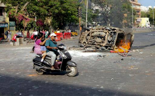 A family on a scooter rides past as a vehicle suspected to be set on fire by protestors (AP Photo)