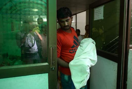 A relative holds the body of a child while walking out of Baba Raghav Das Hospital in Gorakhpur, in Uttar Pradesh/ AFP