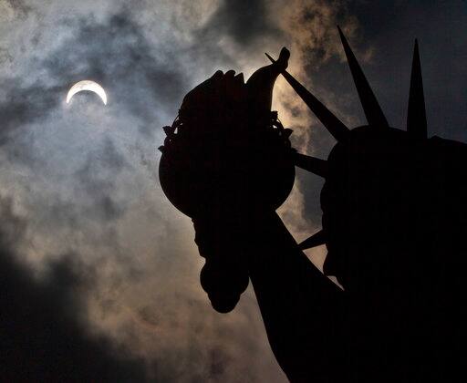A partial solar eclipse appears over the Statue of Liberty on Liberty Island in New York, Monday, Aug. 21, 2017. (AP Photo/Seth Wenig)