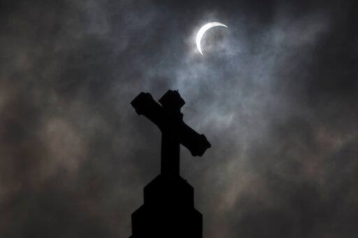Clouds break to show the partial solar eclipse behind the cross of St Mary's Catholic Church in Janesville, Wis., Monday, Aug. 21, 2017. (Anthony Wahl/The Janesville Gazette via AP)