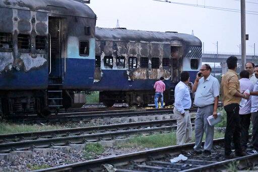 People stand near vandalized train coaches in New Delhi, India, Friday, Aug. 25, 2017. Mobs rampaged across the north Indian town of Panchkula on Friday after a court declared a quasi-religious sect leader guilty of raping two of his followers. Two coaches of an empty train parked in New Delhi's Anand Vihar station were also set on fire. (AP Photo/Manish Swarup)