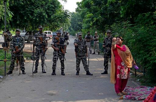 A supporter of the Dera Sacha Sauda religious sect squat others to join her as Indian paramilitary soldiers stand guard on a barricaded road leading to a court in Panchkula, India, Friday, Aug. 25, 2017. Several north Indian cities were under a security lock down Friday as a court was expected to issue a verdict in a rape case involving a man who calls himself Saint Dr. Gurmeet Ram Rahim Singh Ji Insan, the flamboyant leader of the quasi-religious sect. (AP Photo/Altaf Qadri)