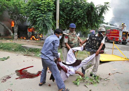 Security officers carry the limp body of a man after Dera Sacha Sauda sect members went on a rampage near a court in Panchkula, India, Friday, Aug. 25, 2017. Deadly riots have broken out in the northern Indian town after a court convicted the sect's guru of raping two of his followers. Mobs also attacked journalists and set fire to government buildings and railway stations. (AP Photo/Kapil Sethi)