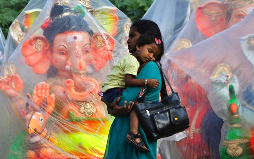 An Indian woman holds a child as she walks past idols of elephant headed Hindu god Ganesha displayed for sale ahead of Ganesh Chaturthi festival in Bangalore, India, Monday, Aug. 21, 2017. After worshipping the idols in their homes or specially set up worship venues, devotees immerse them in water bodies at the end of the festival. (AP Photo/Aijaz Rahi)