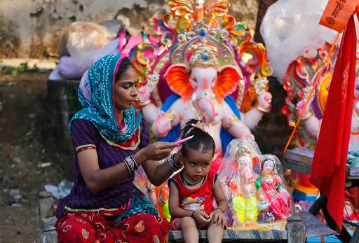 An Indian woman combs the hair of a child as she waits for customers for idols of the elephant-headed Hindu god Ganesha ahead of Ganesh Chaturthi festival in Ahmadabad, India, Thursday, Aug. 24, 2017. The ten-day long Ganesha festival begins Aug. 25. (AP Photo/Ajit Solanki)