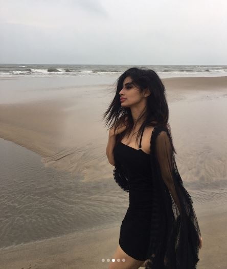 She looked beautiful in a black dress, sitting at a beach. 