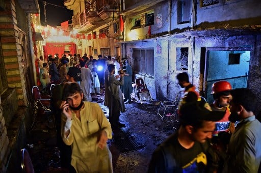 Pakistani security officials and volunteers search the site after a suicide bombing at an election rally in Peshawar / AFP