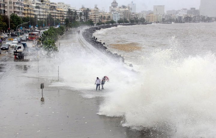  People walk along the shore as a high tide hits the sea wall at Marine Drive, in Mumbai. PTI Photo