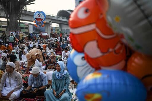 Indonesia: Festive fervor marked the day in Indonesia. A Muslim boy holds a balloon as others gather outside a mosque before Eid al-Adha prayers in Palembang. Image: AFP, Mohd Rasfan