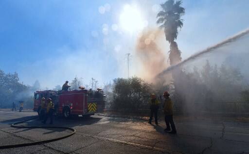 Water from a firetruck douses flames and smoke near homes in West Hills, California, Photo by Frederic J. BROWN / AFP)