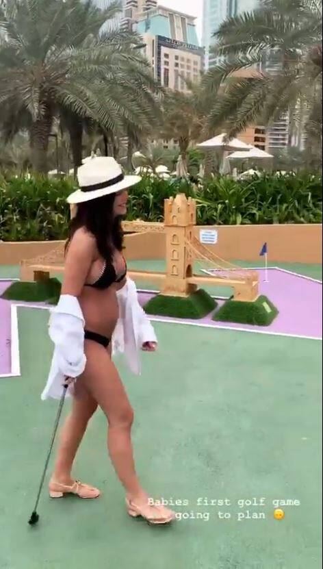 Amy playing golf in a black bikini flaunting her baby bump