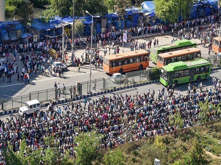 Hordes of people, including women and children, with their bags on their heads and backs many also wearing protective masks - waited in long queues to board buses at the Anand Vihar Interstate Bus Terminal. (Image: PTI) 