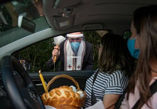 Ukranian descendant priest wears a face mask and shield against the spread of the new coronavirus as he blesses Easter baskets carried by Catholic faithful on their cars in Curitiba, Parana state, Brazil. (Photo: AFP)