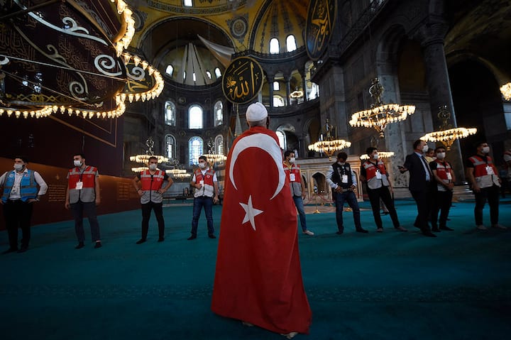  A man draped in a Turkish flag stands as people walk inside the Byzantine-era Hagia Sophia following the inaugural Friday prayers. Critics have said that the President is trying to please nationalistic base in the country. AP/PTI(AP24-07-2020_000215B)