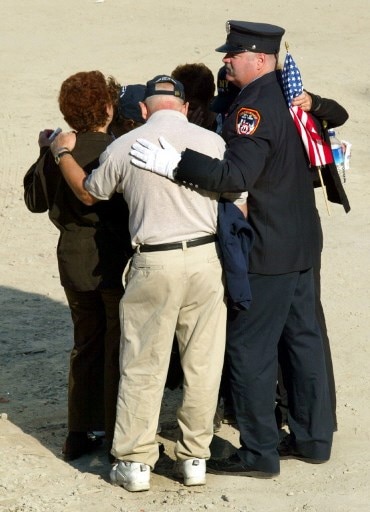 A New York City firefighter and others hug in the pit as mourners pay their respects to lost ones of the World Trade Center attack during the 9/11 Commemoration Event 11 September, 2003, at the World Trade Center site. Image (AFP)