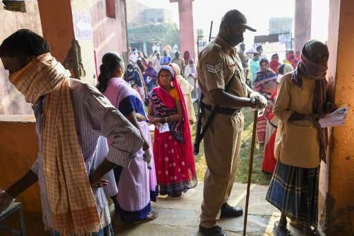 A policeman stands guard as voters queue up to cast their ballots for Bihar state assembly elections at a polling station in Patna. The first phase of voting has started from today. Image (AFP)