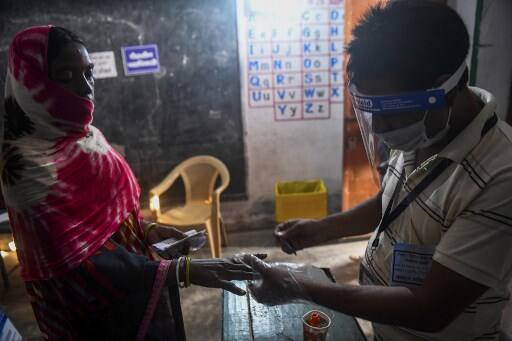 An electoral official (R) wearing a facemask and a shield as a preventive measure against the Covid-19 coronavirus marks a voter's finger with ink after casting her ballot for Bihar state assembly elections in a polling station in Patna.