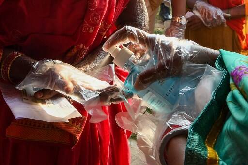 An electoral official sprays sanitiser on the hand of a voter as she waits in a queue to cast her ballot for Bihar state assembly elections at a polling station in Patna