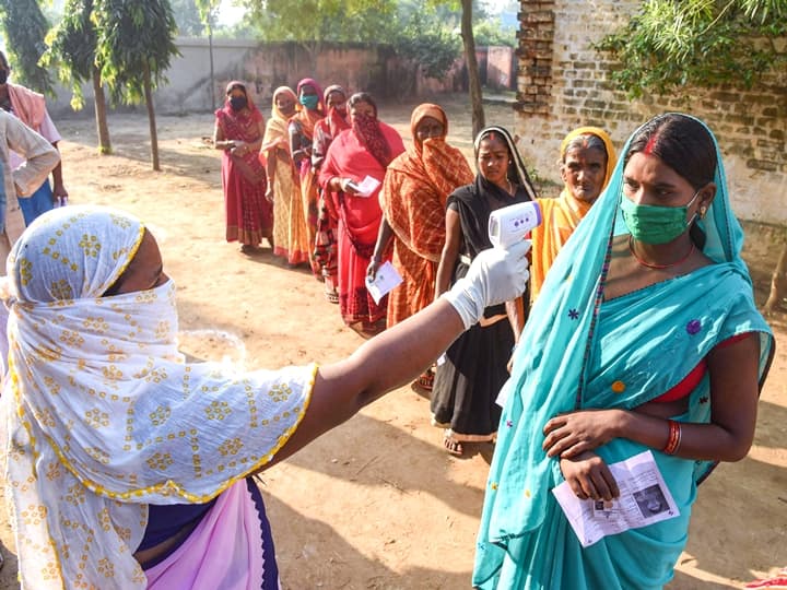 Patna: Voters undergo thermal screening as they stand in a queue outside a polling station to cast their votes for the first phase of Bihar Assembly Elections, at Naubatpur in Patna, Wednesday,  Oct. 28, 2020. (PTI Photo)