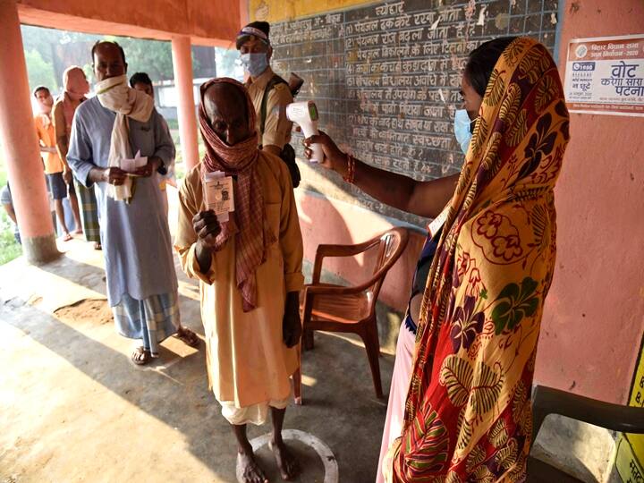 Paliganj : A woman wearing a face mask as a protective measure against the coronavirus screens the body temperature of voters at a polling station, during the first phase of state elections at Paliganj, in the eastern Indian state of Bihar, Wednesday, Oct. 28, 2020.(PTI Photo)