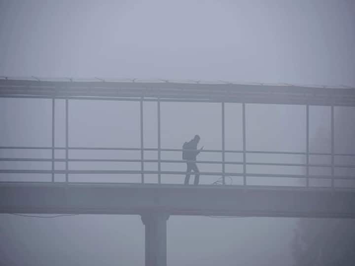 A person walks along a foot over bridge amid dense fog, at Old Delhi road near Bus Stand, in Gurugram. (Photo via Getty Images)