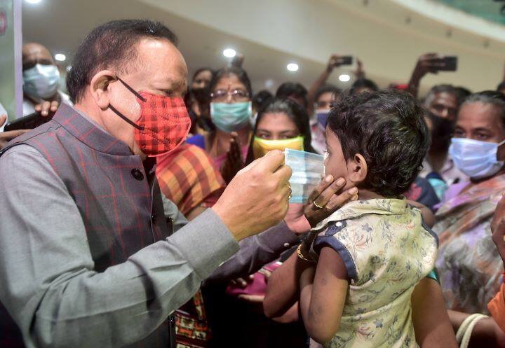 The second phase of nationwide coronavirus (Covid-19) vaccination dry run, the largest such drill undertaken so far, is being conducted across 33 states and Union Territories (UTs) on Friday.
Union Health Minister Harsh Vardhan helps a child wear a mask during his visit to review the  dry run in Chennai. (Image: PTI)