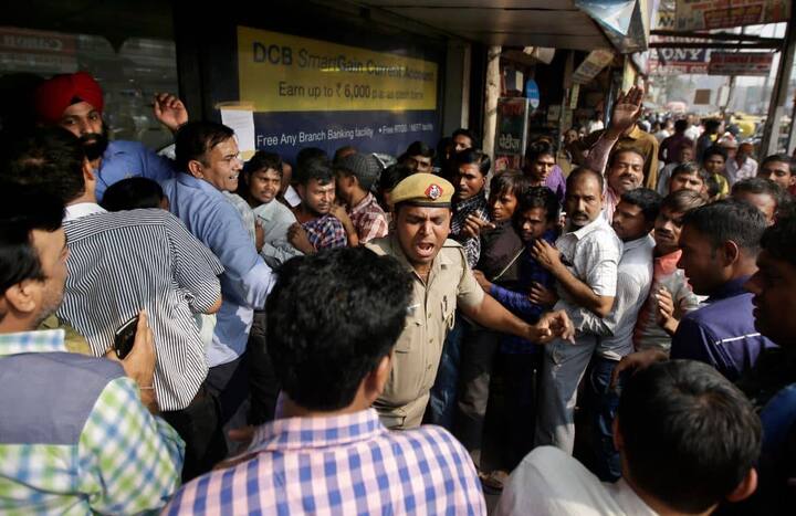 लंबी-लंबी कतारों में घंटो से खड़े लोगों को शांत करता एक पुलिस वाला.