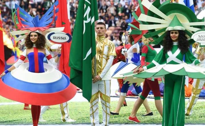 परफॉर्मर्स रूस और सऊदी अरबिया के फ्लैग्स लिए नज़र आ रहे हैं. ऐसा इसलिए भी देखने को मिला क्योंकि जो पहला मैच था वो दोनों देशों के बीच ही था. तस्वीर: एफपी 