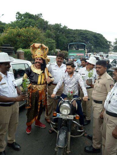  मृत्यु के देवता गदाधारी ‘यमराज’ का रूप धरकर पारंपरिक सुनहरे पोशाक में एक पुलिसकर्मी बेंगलुरु टाउन हॉल के निकट मोटरचालकों को रोककर उन्हें यह चेतावनी देता दिखा कि अगर उन्होंने यातायात नियमों का उल्लंघन किया तो वह उनके घर आयेगा. फोटोः ट्विटर 