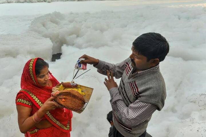 यमुना के गंदे पानी में भी लोगों ने छठ का महापर्व मनाया है. इस तस्वीर में झाग के बीच सूर्यदेव की उपासना कर रहीं व्रती महिला के हाथ में रखी डाली पर एक भक्त अर्घ्य दे रहे हैं.