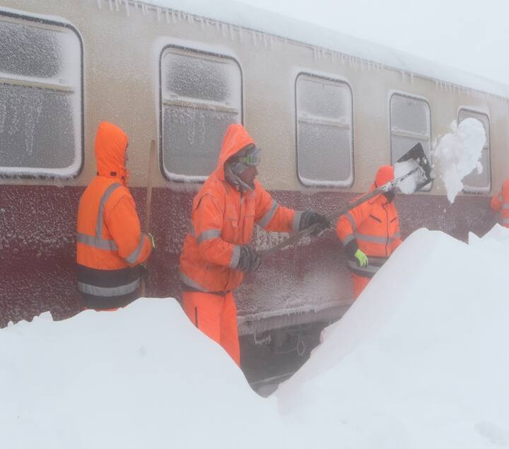 जर्मनी, शियरके: सर्विस कंपनी के कर्मचारी हर्ज़ नैरो-गेज रेलवे की एक ट्रेन से बर्फ हटाने की कोशिश करते हुए जो सोमवार से ब्रोकरन में बर्फबारी में फंसी हुई है. फोटो- Getty Images