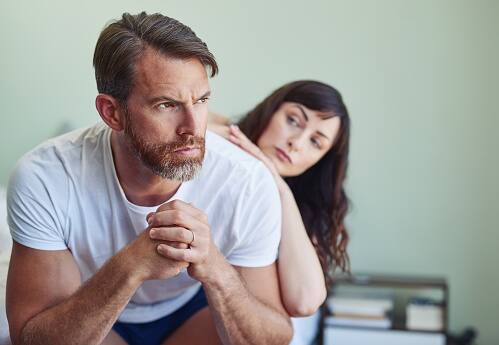 Shot of a unhappy looking middle aged man looking into the distance while his partner tries to comfort him in the bedroom