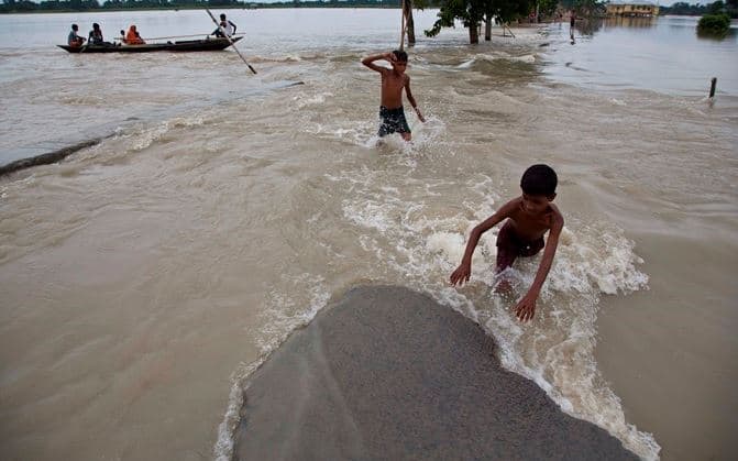 জলাশয় ও রাস্তা এক হয়ে গিয়েছে। তারই মধ্যে দিয়ে চলেছে বাচ্চারা।