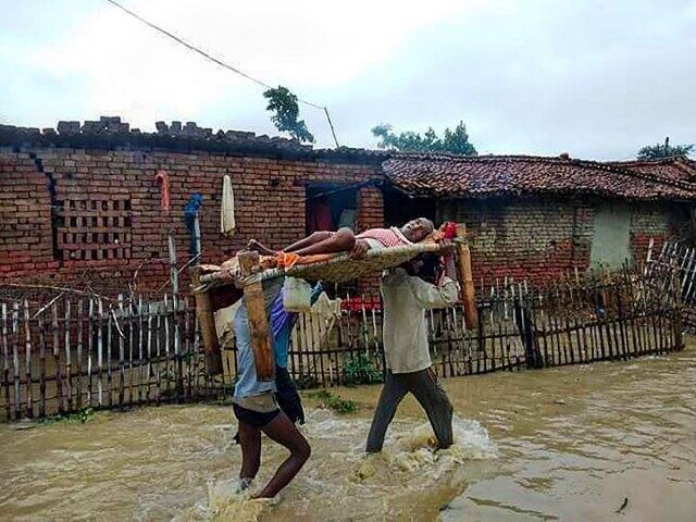 পূর্ব চম্পারনে বানভাসি একটি গ্রামে এক রোগীকে ডুলিতে চাপিয়ে হাসপাতালে নিয়ে যাওয়া হচ্ছে। গত ২৪ ঘন্টায় সমস্ত বড় নদীর জল বিপদসীমার ওপর দিয়ে বইছে। এরফলে বাঁধ ভেঙে যাওয়ার ঘটনা ঘটেছে। ছবি-পিটিআই