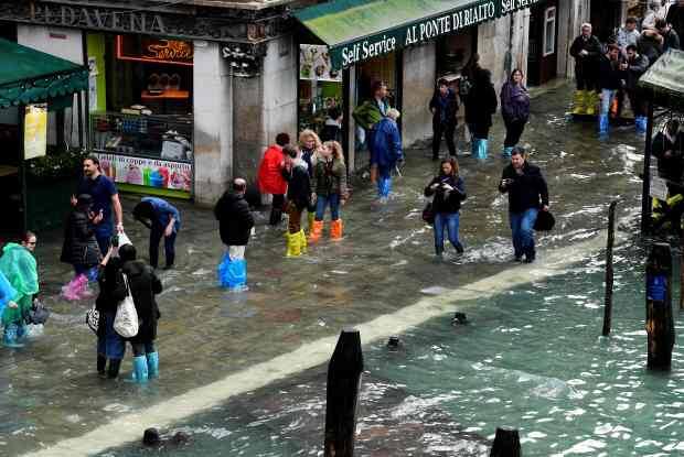 Tourists walk in the flooded street near Rialto Bridge during a acqua-alta (high-water) alert in Venice on October 29, 2018. - The flooding, caused by a convergence of high tides and a strong Sirocco wind, reached around 150 centimetres on October 29. (Photo by Miguel MEDINA / AFP)MIGUEL MEDINA/AFP/Getty Images
