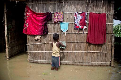 In this July 5, 2017, file photo, an Indian boy dries clothes outside his house, partially submerged in flood waters at Burgaon, 80 kilometers (50 miles) east of Gauhati, Assam state, India, Wednesday, July 5, 2017. Heavy rains since the start of India's monsoon season have triggered floods and landslides in parts of the remote northeastern region, causing at least 20 deaths, authorities said Wednesday. (AP Photo/Anupam Nath, File)